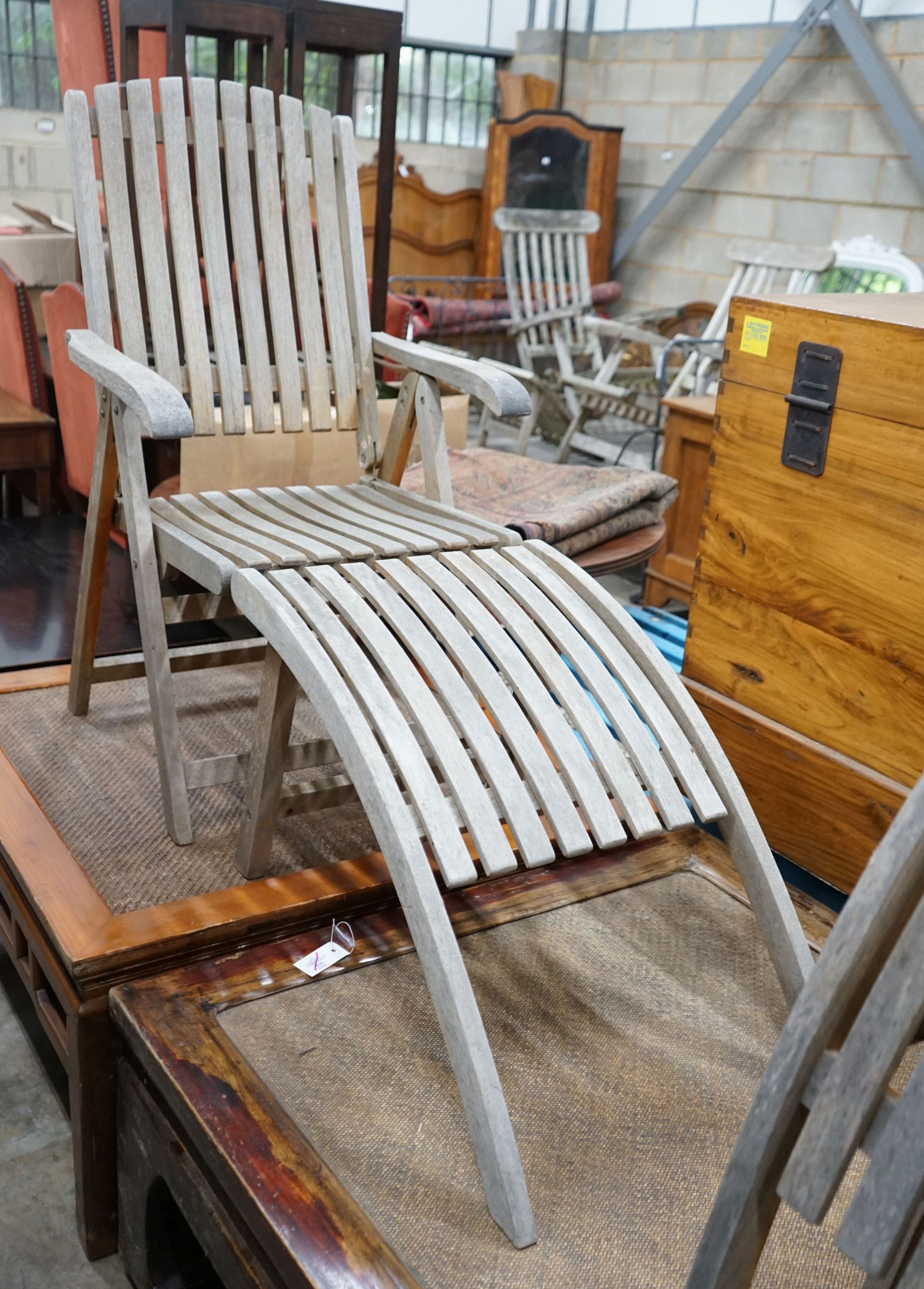 A pair of weathered teak folding reclining garden elbow chairs with footrests and seat pads